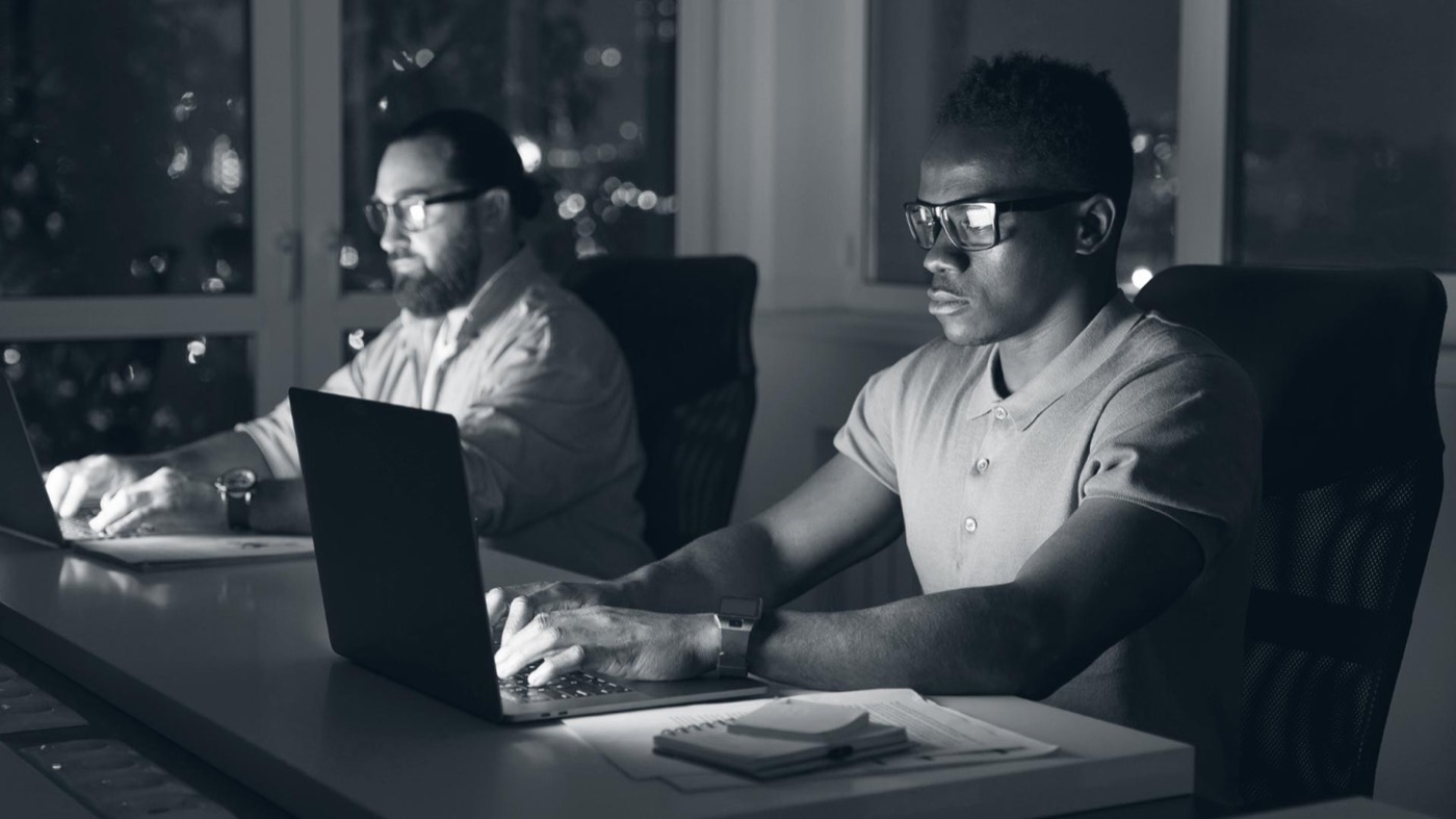 Two engineers reviewing network activity on their laptops in a dark office